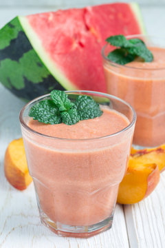 Watermelon, peach, mint and coconut milk smoothie in glass on white wooden background, vertical
