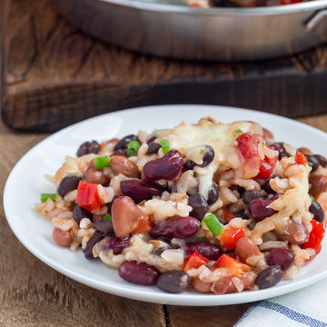 Baked rice casserole with black beans, pinto beans, kidney beans and cheese, on white plate, square format