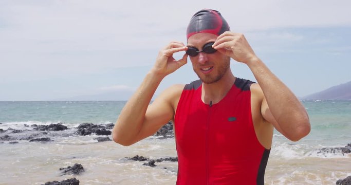 Triathlon man going swimming - male triathlete swimmer adjusting swim goggles getting ready for the challenge of an ocean swim. Fit man in professional triathlon suit training for ironman on Hawaii.