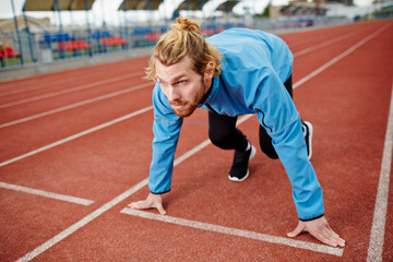 Fototapeta premium Determined young man in sportswear waiting for start signal during run competition