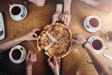 Top view of hands taking pizza slices from a plate standing on a table with tea cups around