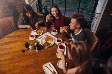 High angle shot of group of best friends having dinner at round table together talking and smiling in cozy cafe