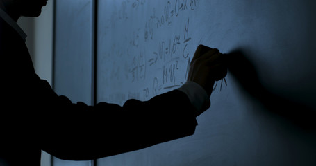 Scientist writing formulas on chalkboard. Hand with chalk wrote physics formulas on black chalkboard closeup