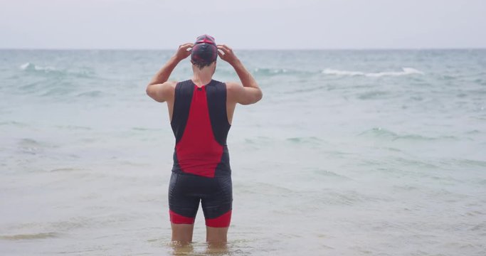 Concentration, determination and focus. Triathlon athlete man ready for challenges, swimming in ocean. Male triathlete adjusting swimming goggles going for swim training for goal: Ironman.