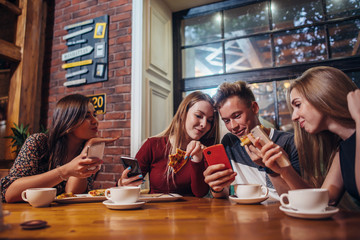 Young people using their mobile phones sitting around the table having a meal in modern stylish cafe