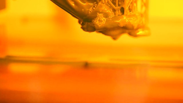 Stereolithography DPL 3d printer create detail and liquid drips, platform slowly move with liquid close-up. Progressive modern additive technology 3D printing, create scaled model by UV polymerization