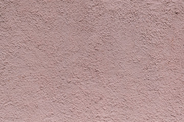 The rough texture of the decorative plaster on the wall. The surface of pink or beige with drips, drops and cracks. There are dimples and bumps.