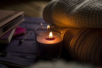 warmth and comfort: a sweater, books and candle on a wooden table