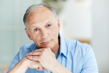 Calm retired man leaning on his hands and looking at camera
