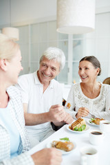 Three senior friends sitting by festive table, eating tasty cake and talking