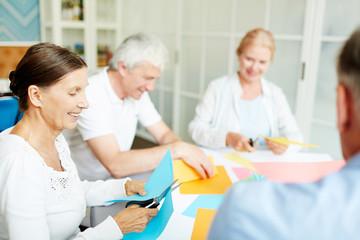 Group of friendly seniors cutting colorful paper to create figures