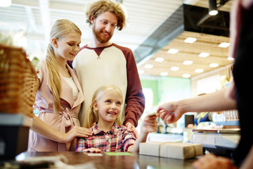 Little girl giving card to shop assistant with her parents standing near by