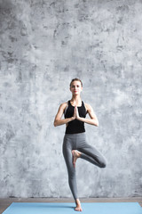 Fototapeta na wymiar Young woman practicing yoga vrikshasana in gym.