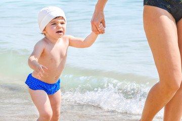 baby walk hand in hand with mother - newborn at the sea with mom - child tantrums on the beach