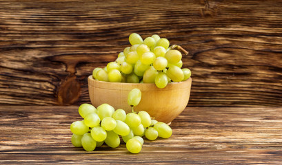 Bowl with fresh ripe green grapes on wooden background.