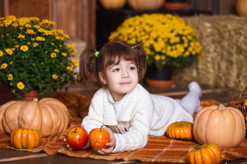 Portrait of adorable smiling girl posing with orange pumpkin in fall wooden interior.