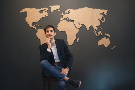 Young man looking to world map with crossed hands
