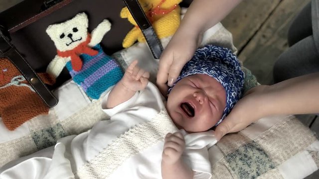 Baby and hands of woman. Infant in knitted hat crying. Child care tips.