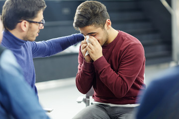 Friendly psychologist reassuring lonely young man in tears during session