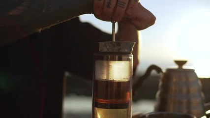 footage of concentrated man in black t-shirt with tattoo on his arm brewing ground coffee in glass french press early in morning slow motion