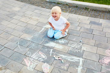 Fototapeta premium Little boy drawing with chalks on asphalt