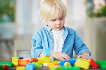 Little boy playing with colorful plastic construction blocks