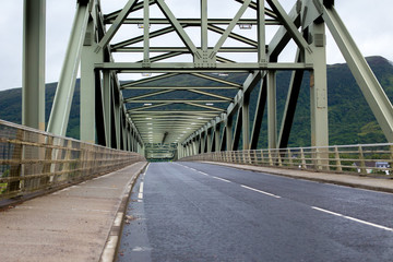 Fototapeta na wymiar Wet road under a steel bridge front of a Scottish mountain