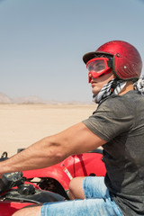 Young guy during desert excursion by quad - Man in helmet and adventure clothes in exotic scenarios...