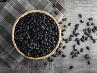 Black beans in a wooden bowl, black beans in a wooden spoon on a wood background