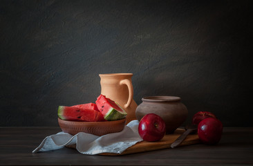 Rustic still life. A set of pottery, red apples and a watermelon on a wooden table © symbol344