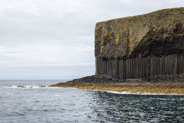 Natural geometric dark stone cliff of Scottish Island in the sea