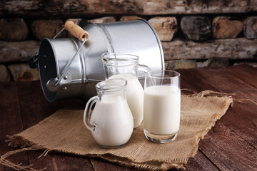 A jug of milk and glass of milk on a wooden table - obrazy, fototapety, plakaty