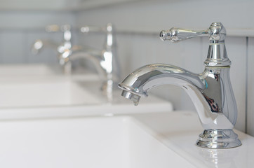 silver faucet or water tap with white washing sink in public toilet.