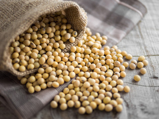 Soy beans in a wooden bowl on wooden background with sack, soy beans on wooden spoon with sack.