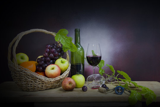 A basket of grapes and variety of fruits with a bottle and glass of wine on the old wooden  table, still life image.