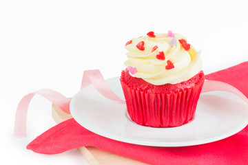 Red Velvet Cup Cake topped with red, purple, pink heart shaped icing on white background over wood board & red napkin with ribbon for special holiday celebration, Valentines day or Christmas occasions