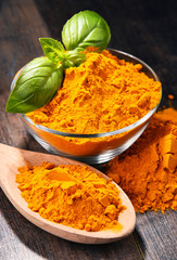 Composition with bowl of turmeric powder on wooden table