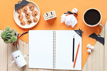 Halloween, celebration or holiday background concept : Mock up of open notebook, paper crafts, cube calendar, grilled carrots with scary face and coffee cup, Top view or flat lay with copy space