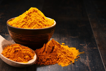 Composition with bowl of turmeric powder on wooden table