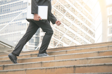 Businessman holding laptop step up on stair to future with building background in city outdoor