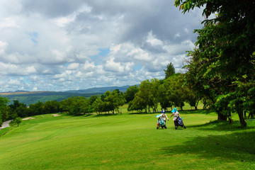 golfer walking with caddies in golf course with view of mountain and blue sky and cloud in sunny day