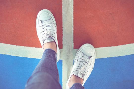 Women's legs in white sneakers are standing on the choice of whether to go left or right.