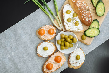 Obraz na płótnie Canvas Top view of a crusty baguette slices with cherry tomatoes, cucumbers and green olives, cream cheese, healthy breakfast or snack on a wooden board