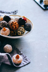 Raw chocolate candy with nuts, figs and citrus, truffle in white plate on a grey background. Healthy vegan dessert.