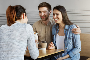 Beautiful guy with dark hair introduces his girlfriend to friend, they laughing, eating sandwiches, having good time together.