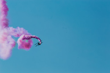 Aerobatic plane leaving a pink smoke trail in the blue sky.