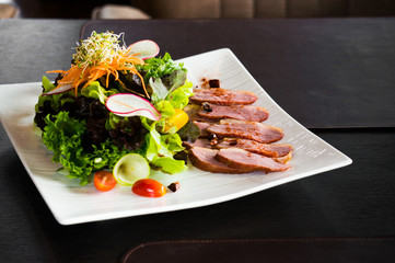 Grilled duck salad on white plate on black table for dinner