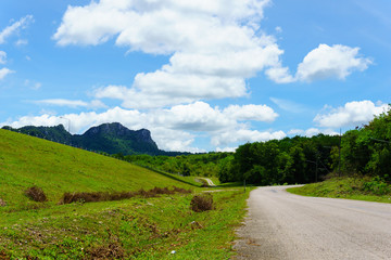 empty asphalt country road along the wall of dam with green grass and blue sky with clouds and mountain background in countryside