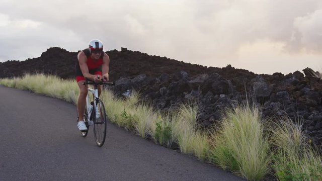 Cycling Triathlon man - male triathlete biking on triathlon bike. Fit man cyclist on professional triathlon bicycle wearing tri suit and time trail helmet training for ironman. From Big Island, Hawaii