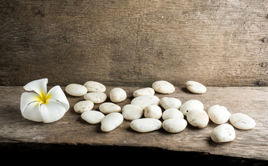 White flower and leafs with big and tiny stone and towel on wood table for health spa advertisement and presentation